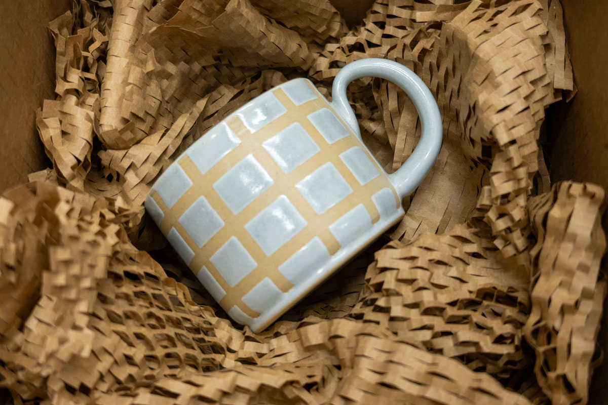 Ceramic mug on a bed of honeycomb wrapping paper inside a box